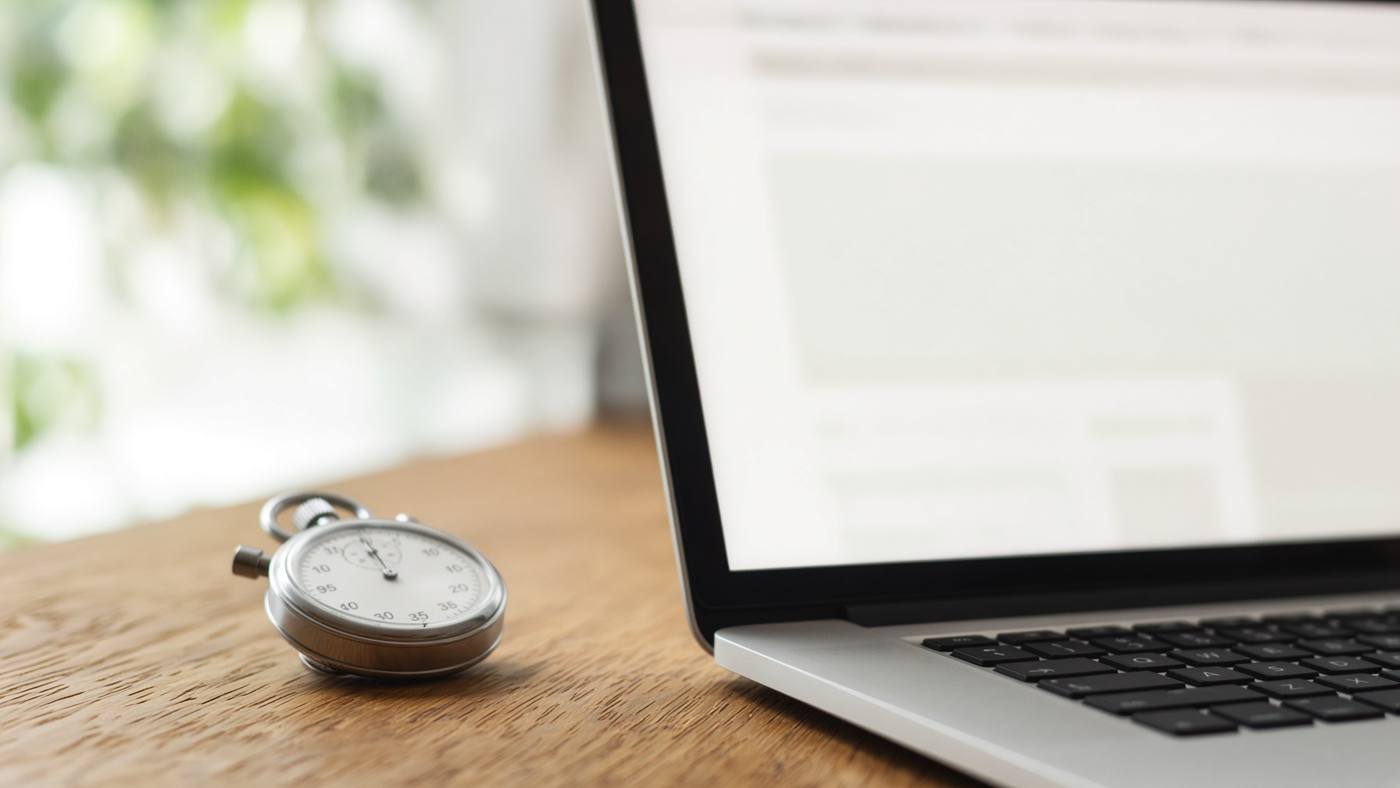 A laptop and stopwatch on oak, reviewing WordPress speed and Core Web Vitals
